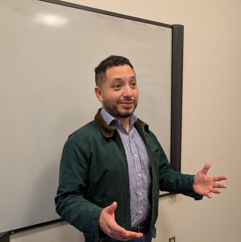 Contact 1 Edgar Garcia a licensed agent is standing in front of a whiteboard with arms out in the middle of a presentaion