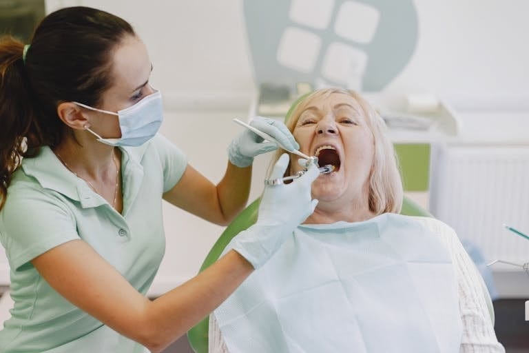 A female dentist examines a senior woman patient in a dental clinic setting. what Medicare doesn't cover in 2026 including dental and long-term care.
