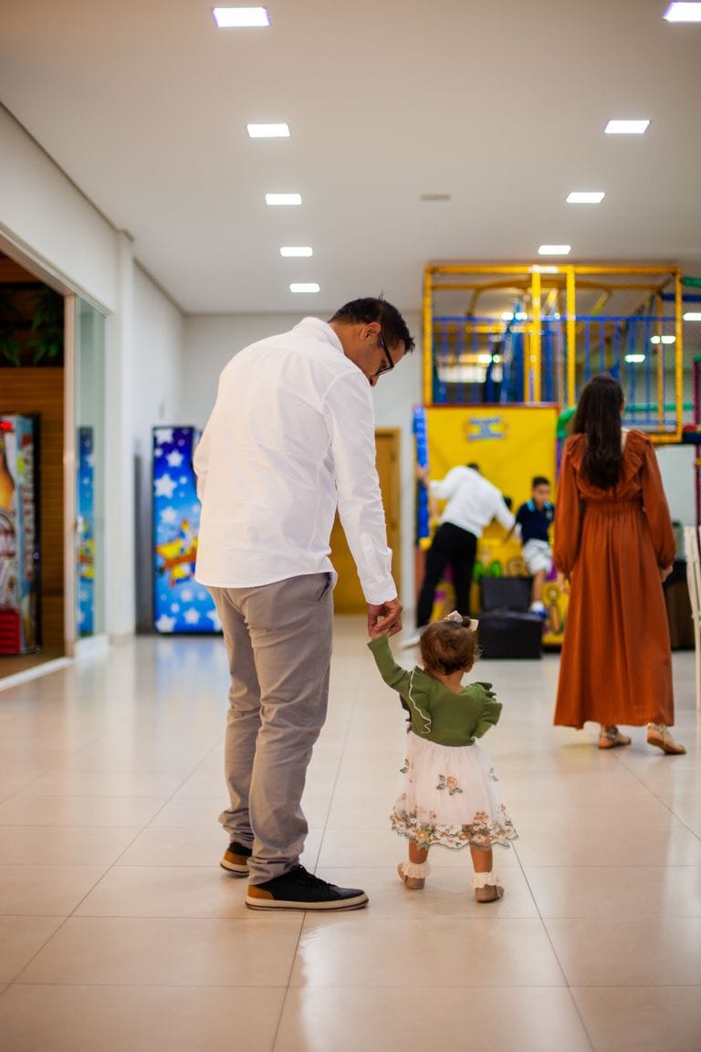 A father and his young daughter walking hand in hand inside a colorful play area in Paraná, Brazil.